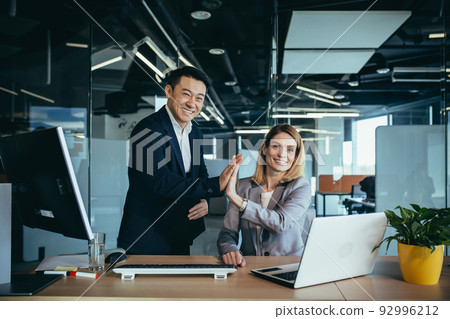A team of employees, a man and a woman business people, working in the office, rejoicing in success, clapping together A team of employees, a man and a woman business people, working in the office, rejoicing in success, clapping together 92996212