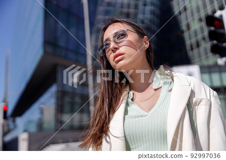 Attractive woman in trendy outfit standing on skyscrapers cityscape background and looking away Attractive woman in trendy outfit standing on skyscrapers cityscape background and looking away 92997036