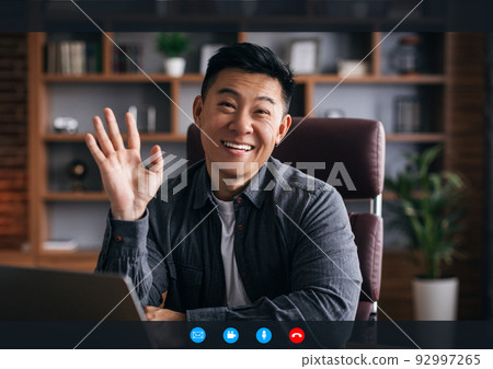 Cheerful mature chinese man with laptop waving hand at camera in room interior on device screen with buttons 92997265