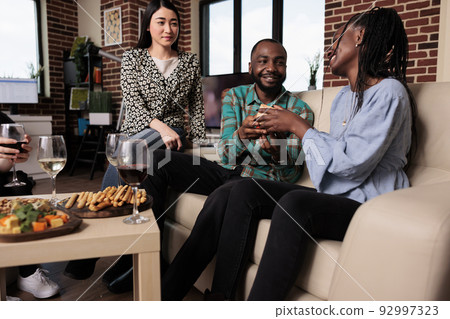 Interracial people enjoying time together while giving each other gifts and drinking alcoholic beverages. Diverse group of friends celebrating birthday at wine party while exchaning gifts. Interracial people enjoying time together while giving each other gifts and drinking alcoholic beverages. Diverse group of friends celebrating birthday at wine party while exchaning gifts. 92997323