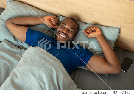 Cheerful African Guy Stretching After Sleep Lying In Bed Indoor 92997332