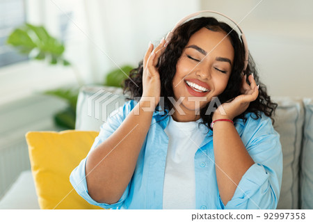 Happy Black Lady Listening Music Wearing Headphones Sitting At Home Happy Black Lady Listening Music Wearing Headphones Sitting At Home 92997358