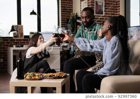 Diverse people celebrating friendship event while having wine party at home. Multiethnic group of cheerful friends clinking wine glasses while toasting and drinking alcoholic beverages. Diverse people celebrating friendship event while having wine party at home. Multiethnic group of cheerful friends clinking wine glasses while toasting and drinking alcoholic beverages. 92997360
