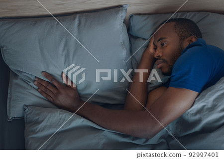 Unhappy Black Man Touching Pillow Lying In Bed Indoor Unhappy Black Man Touching Pillow Lying In Bed Indoor 92997401