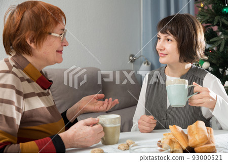 Two women drink tea and eat cakes near the New Year tree.  93000521