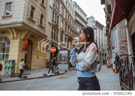woman wearing sweater drinking her coffee while standing 93002340
