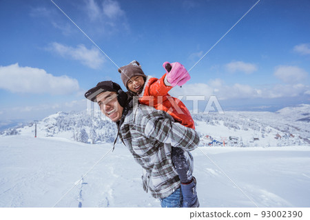 father piggyback ride with daughter while playing outside in snow 93002390