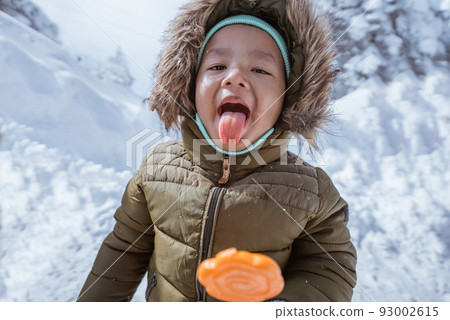 kid enjoying lollipop outside during snowy winter kid enjoying lollipop outside during snowy winter 93002615