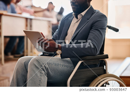 Close-up of African teacher with disability sitting on wheelchair and using digital tablet during lecture Close-up of African teacher with disability sitting on wheelchair and using digital tablet during lecture 93003647