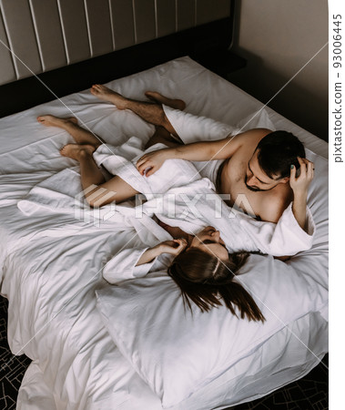 Top view of young couple in love in bathrobes lying in bed and cuddling 93006445