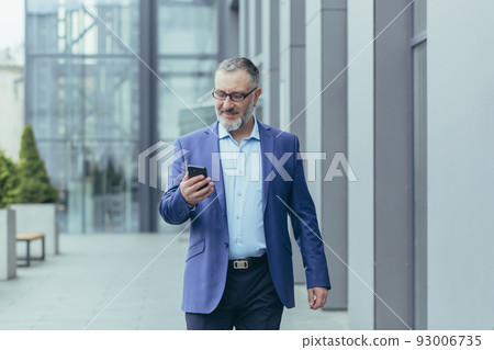 Successful and happy senior gray-haired businessman investor walking outside office building, man holding phone, banker using smartphone, typing message and reading news 93006735
