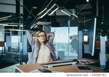 business owner woman resting during working hours puts her hands behind her head, thinks about business plans, works in a modern office 93006763