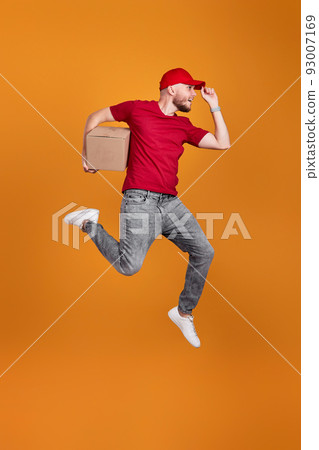 Delivery man in red cap holding cardboard box and jumping 93007169