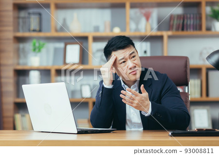 Businessman worried about business, sad and frustrated sitting in the office, looking anxiously at the laptop screen Businessman worried about business, sad and frustrated sitting in the office, looking anxiously at the laptop screen 93008811
