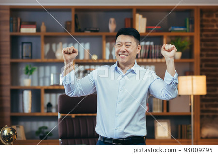 Happy businessman dancing and celebrating victory sitting at a table in a classic office, Asian working at computer Happy businessman dancing and celebrating victory sitting at a table in a classic office, Asian working at computer 93009795