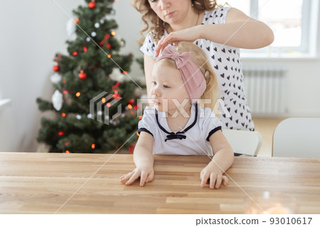 Mother fixing her daughter's cochlear implant hearing aid on christmas tree background - deafness and diversity concept. Innovative technologies i 93010617