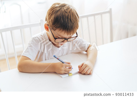 A boy in eyeglasses writes with a pen in a notebook A boy in eyeglasses writes with a pen in a notebook 93011433