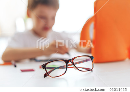 Glasses in front of a child watching a video lesson on a tablet Glasses in front of a child watching a video lesson on a tablet 93011435