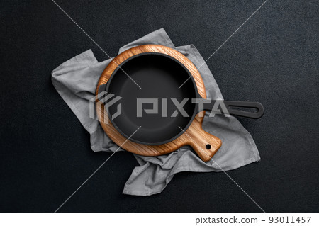 Cast iron skillet on a wooden board. Frying pan, cutting board and kitchen towel on a black background. Kitchen utensils. Empty place. Top view. Cast iron skillet on a wooden board. Frying pan, cutting board and kitchen towel on a black background. Kitchen utensils. Empty place. Top view. 93011457