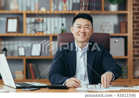 Portrait of a successful Asian banker, businessman working in the office, looking at the camera and smiling, counting metal coins on the table 93011590
