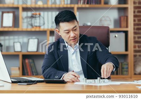An Asian banker works in a classic office at a table, counting coins made of precious metals 93011610