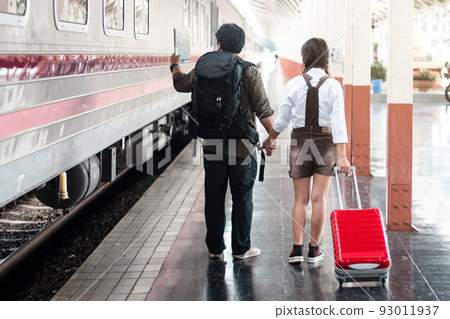 Couple lovers tourist Hold hands with each other hold a map in at in a train station carrying her trolley red bag,traveler with backpack in summer Holiday concept Thailand 93011937