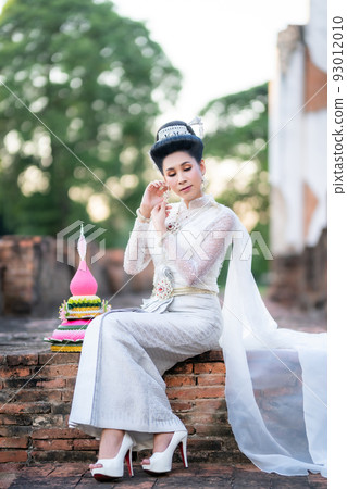 Portrait Beautiful asian woman with Thai white traditional dress costume holding Krathong and sitting in front of Pagoda temple at the ancient city Thailand,Loy Krathong Festival,Transgender model 93012010