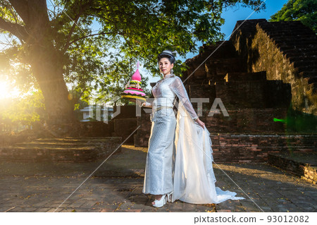 Portrait Beautiful asian woman with Thai white traditional dress costume holding Krathong and sitting in front of Pagoda temple at the ancient city Thailand,Loy Krathong Festival,Transgender model 93012082