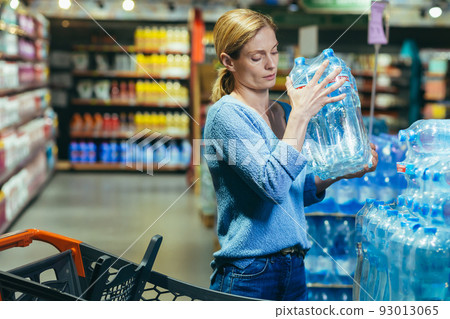 A frightened and sad woman in a crisis buys water in a supermarket, stocks up on drinking water A frightened and sad woman in a crisis buys water in a supermarket, stocks up on drinking water 93013065