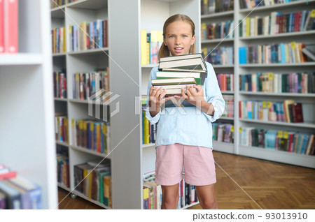 Discontented pupil holding a stack of books in her hands Discontented pupil holding a stack of books in her hands 93013910