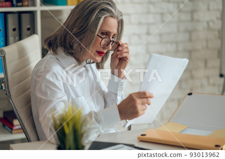 Gray-haired woman looking surprised while reading something Gray-haired woman looking surprised while reading something 93013962