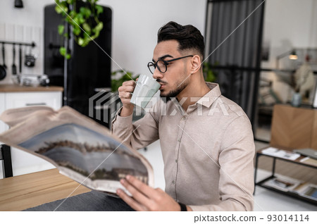 Man drinking coffee reading newspaper sideways to camera Man drinking coffee reading newspaper sideways to camera 93014114