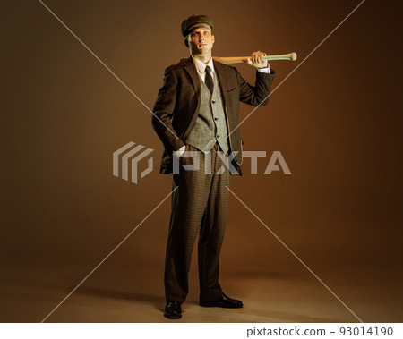 Retro style portrait of young man in image of english gangster, businessman wearing suit and cap standing isolated over dark vintage background. Retro style portrait of young man in image of english gangster, businessman wearing suit and cap standing isolated over dark vintage background. 93014190
