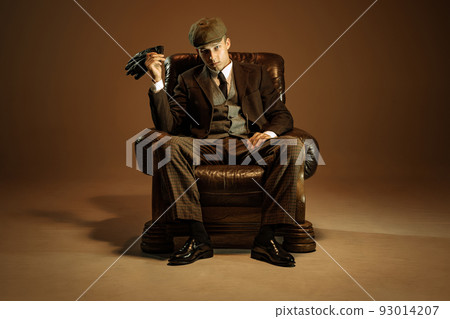 Cinematic portrait of young man, retro 1920s style english gangster wearing suit and cap isolated over dark vintage background. Business, family, art, fashion 93014207