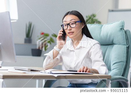 Successful business woman working in modern office, Asian woman talking on the phone, female worker wearing white shirt. Successful business woman working in modern office, Asian woman talking on the phone, female worker wearing white shirt. 93015115