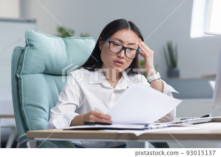 Asian business woman behind paper work, tired and frustrated, working in office, female employee in bra looking at documents and financial reports. Asian business woman behind paper work, tired and frustrated, working in office, female employee in bra looking at documents and financial reports. 93015137