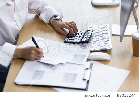 Close-up photo of a business woman's hand on paper work, an accountant calculates and summarizes the results of the financial year with a calculator, an Asian woman works in the office. Close-up photo of a business woman's hand on paper work, an accountant calculates and summarizes the results of the financial year with a calculator, an Asian woman works in the office. 93015244