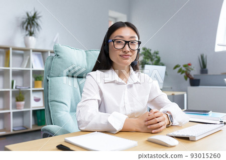 Young tech support worker, portrait Asian business woman working in modern office at work, looking at camera, using headset for video communication. Young tech support worker, portrait Asian business woman working in modern office at work, looking at camera, using headset for video communication. 93015260