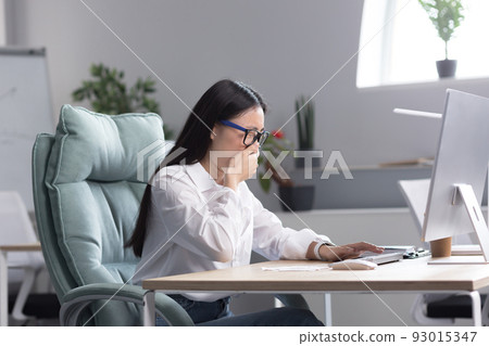Sick Asian female office worker, has cold and flu, coughs and sneezes into tissue, works at computer. Sick Asian female office worker, has cold and flu, coughs and sneezes into tissue, works at computer. 93015347