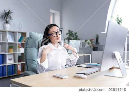 Heat in the office, Asian woman trying to freshen up, business woman working at the computer, waving her hands to cool down. Heat in the office, Asian woman trying to freshen up, business woman working at the computer, waving her hands to cool down. 93015348