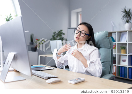 Heat in the office, Asian woman trying to freshen up, business woman working at the computer, waving her hands to cool down. Heat in the office, Asian woman trying to freshen up, business woman working at the computer, waving her hands to cool down. 93015349