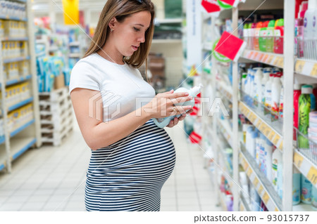 Baby care products pregnancy woman shopping. Young pregnant woman buying on baby bath shampoo bottle on supermarket background. Baby washing powder supermarket choice. 93015737