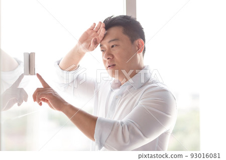 Asian businessman in office heat, chooses cooling mode of air conditioner on control panel on white wall 93016081