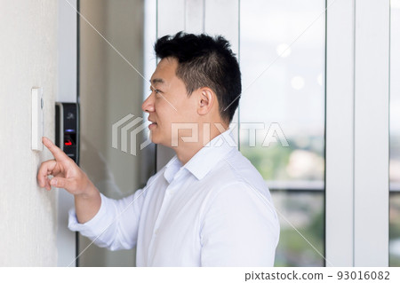 Asian man uses a door knocker with a video camera to open the door. Asian man uses a door knocker with a video camera to open the door. 93016082