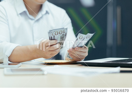 Close-up photo of the hands of a businessman man in a shirt counting money dollars cash, a businessman works in a modern office Close-up photo of the hands of a businessman man in a shirt counting money dollars cash, a businessman works in a modern office 93016870