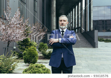 Portrait of successful thinking experienced senior businessman, gray haired male boss in business suit outside office, looking at camera with crossed arms Portrait of successful thinking experienced senior businessman, gray haired male boss in business suit outside office, looking at camera with crossed arms 93018576