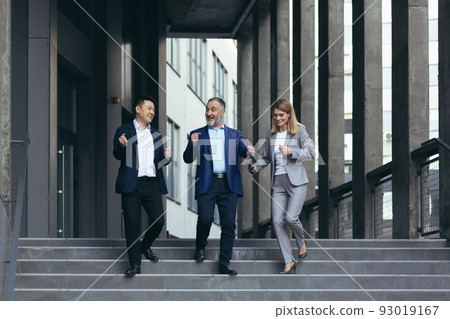 diverse business team, man and woman walking together outside office building, satisfied with victory celebrating, business people dancing on stairs and smiling happy 93019167