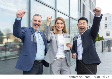 Successful diverse business team, business people looking at camera and rejoicing in success and victory, man and woman holding hands up outside office Successful diverse business team, business people looking at camera and rejoicing in success and victory, man and woman holding hands up outside office 93019173