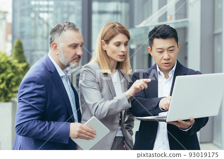 Diverse group of business people, male and female, together outside office brainstorming solutions, team of colleagues looking at laptop screen thinking about business strategy Diverse group of business people, male and female, together outside office brainstorming solutions, team of colleagues looking at laptop screen thinking about business strategy 93019175