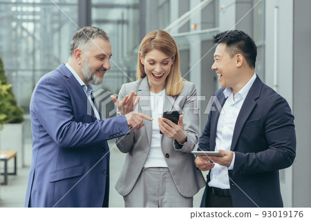 Diverse business team, male and female business people together outside office, group of successful business people looking at colleague's phone, smiling and happy Diverse business team, male and female business people together outside office, group of successful business people looking at colleague's phone, smiling and happy 93019176